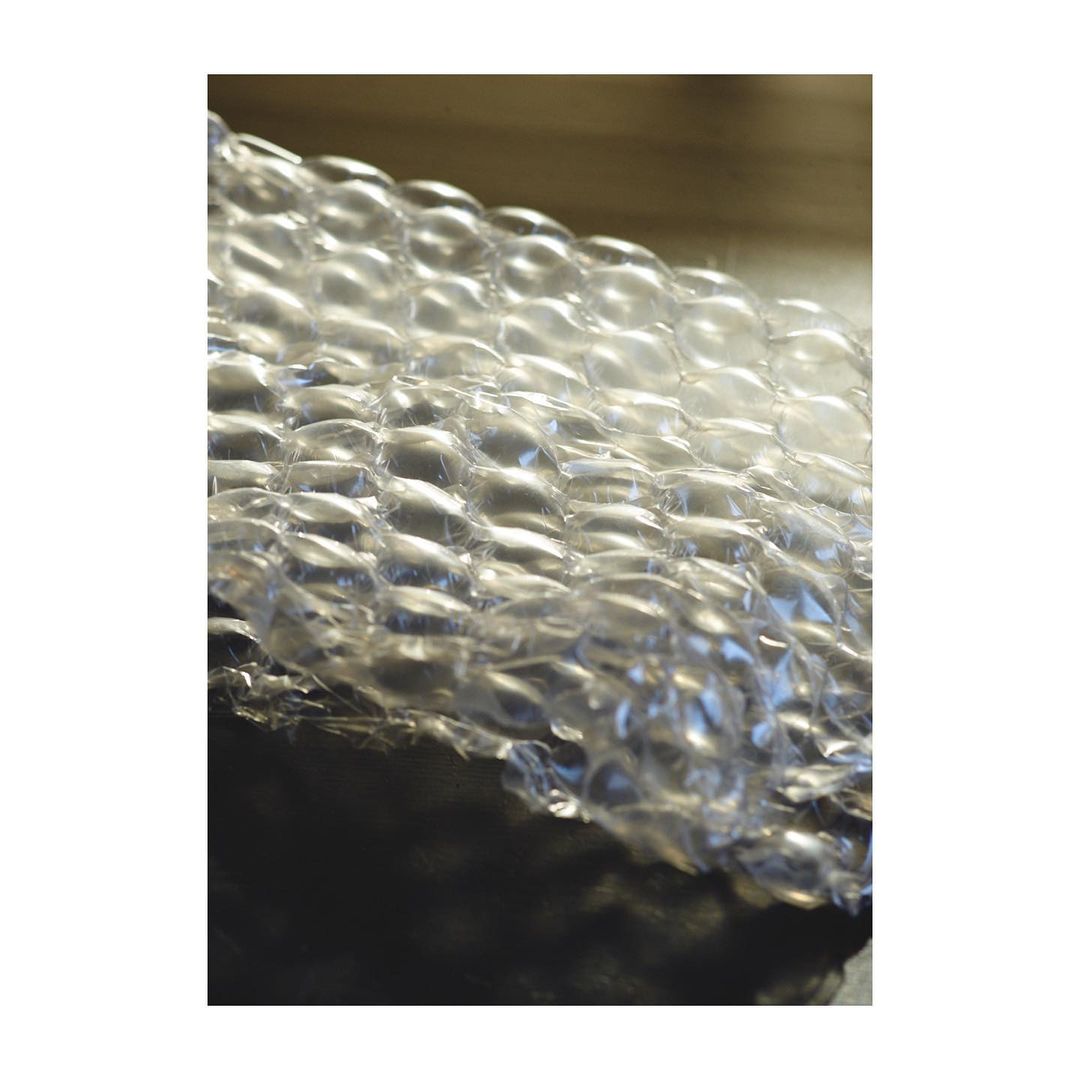 Close-up shot of clear bubble wrap with visible air bubbles. The texture is shiny and reflective, with dark shadows creating contrast.