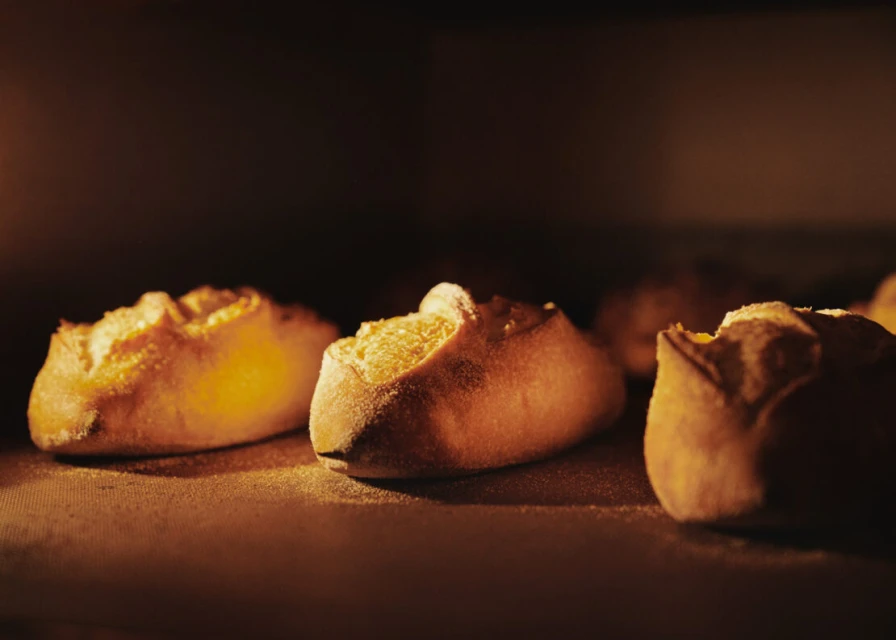 Close-up view of several golden-brown bread rolls baking in a warm-toned oven with a dark background, focus on texture and form.