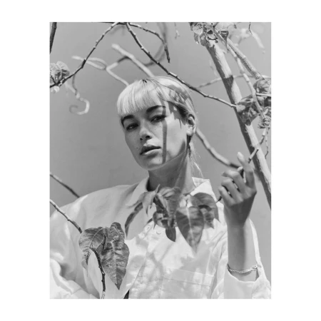 Monochrome portrait of a woman with bangs standing among bare branches and foliage, photographed by Clayton Cotterell.