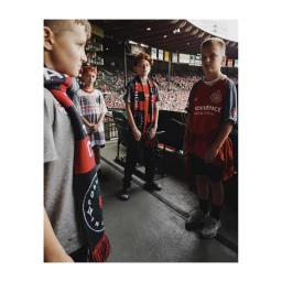 Four young boys in soccer jerseys and scarves standing together in a stadium walkway by Clayton Cotterell