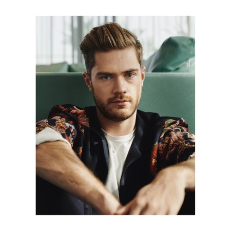Portrait of a man in his 20s with short styled brown hair wearing a patterned silk shirt over a white t-shirt.