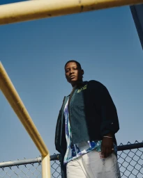 Portrait of a man in a dark jacket and white trousers against a clear blue sky by Clayton Cotterell