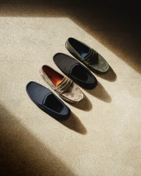 Four pairs of slip-on loafers arranged diagonally on a textured concrete surface under warm sunlight.