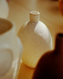 Close-up of a textured ceramic vase with a porous surface surrounded by other pottery pieces.