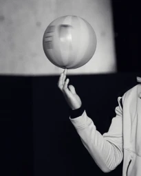 Person spinning a striped ball on their fingertip in a monochrome studio portrait
