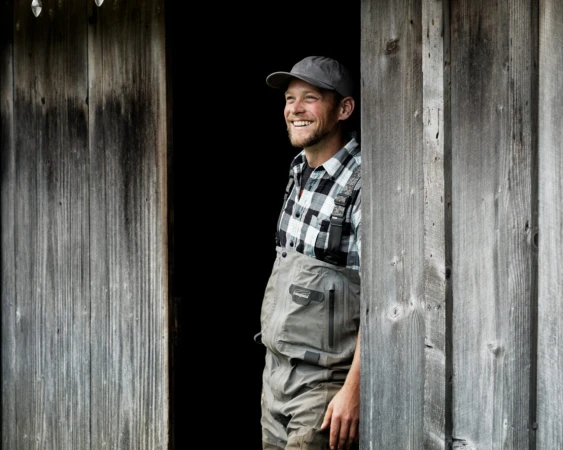 Smiling man in plaid shirt and grey waders peeking from wooden doorway