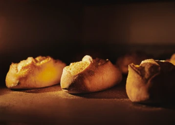 Several small artisanal bread loaves baking inside a dark oven under warm interior light, captured by Clayton Cotterell.