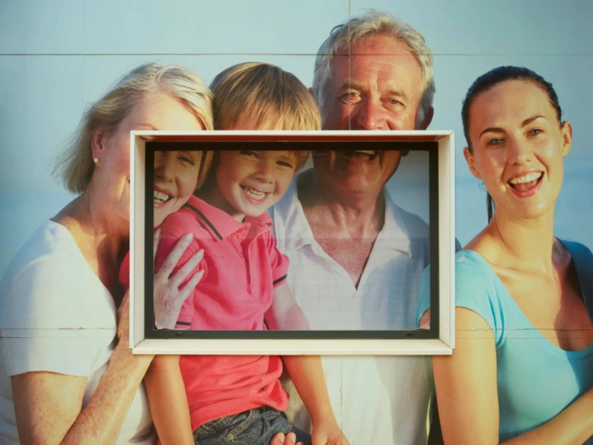 Smiling family portrait featuring two adult women, an adult man, and a child in front of an out-of-focus ocean and beach backdrop.