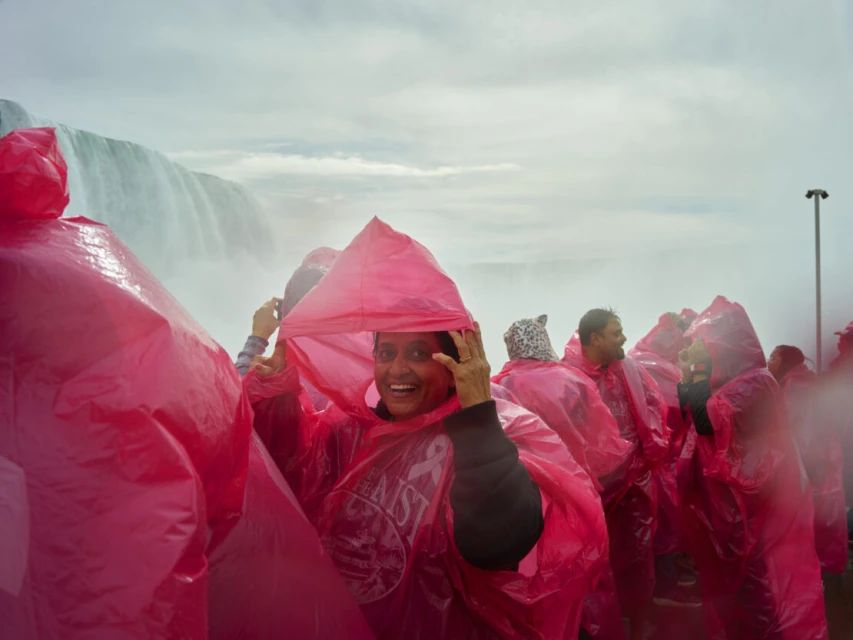 Smiling woman wearing a pink poncho at Niagara Falls with a group of people in pink ponchos and the waterfall in the background.