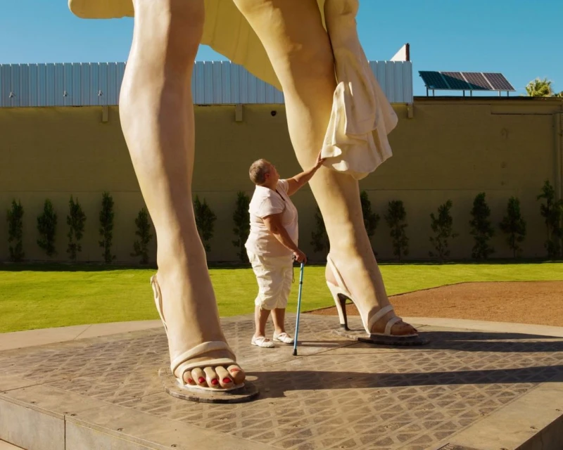 A tourist interacts with the giant Marilyn Monroe statue in Palm Springs; an elderly woman in white touches Marilyn's billowing skirt.