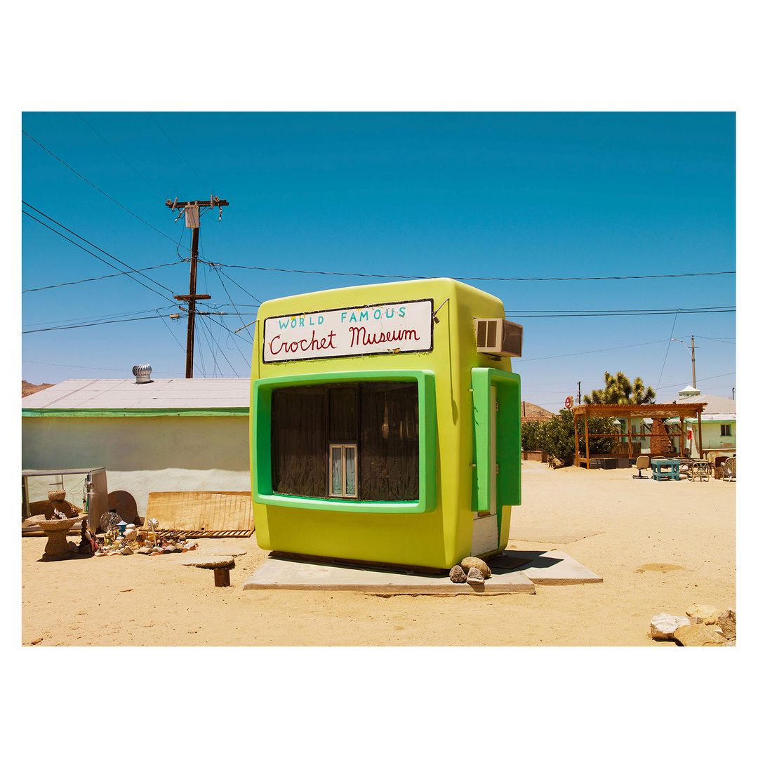 Outdoor shot of the World Famous Crochet Museum in Joshua Tree, California, featuring a bright green building in a desert landscape under a clear blue sky.