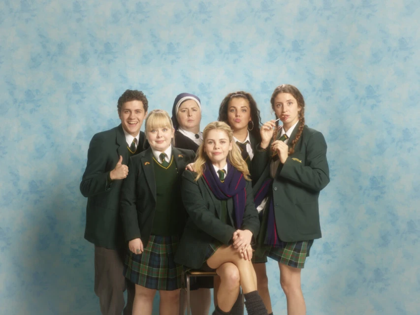 Group portrait of six individuals in school uniforms against a blue backdrop, capturing a playful, editorial style reminiscent of a school photo.