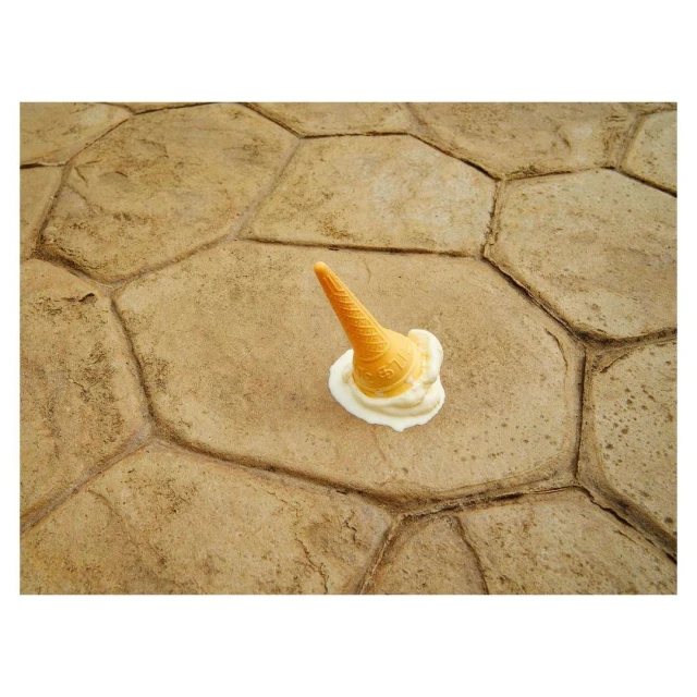 An overturned ice cream cone melts on a tan, patterned stone surface, creating a visually striking and whimsical image.