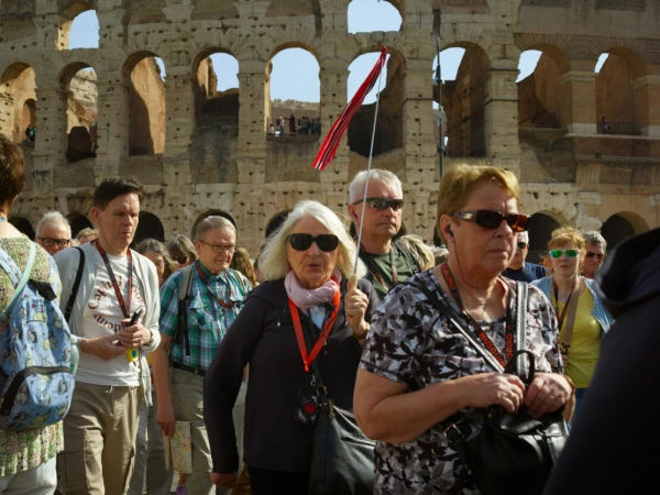 Tourists visit the Colosseum in Rome on a sunny day, exploring the ancient amphitheater with a tour guide holding a red flag.