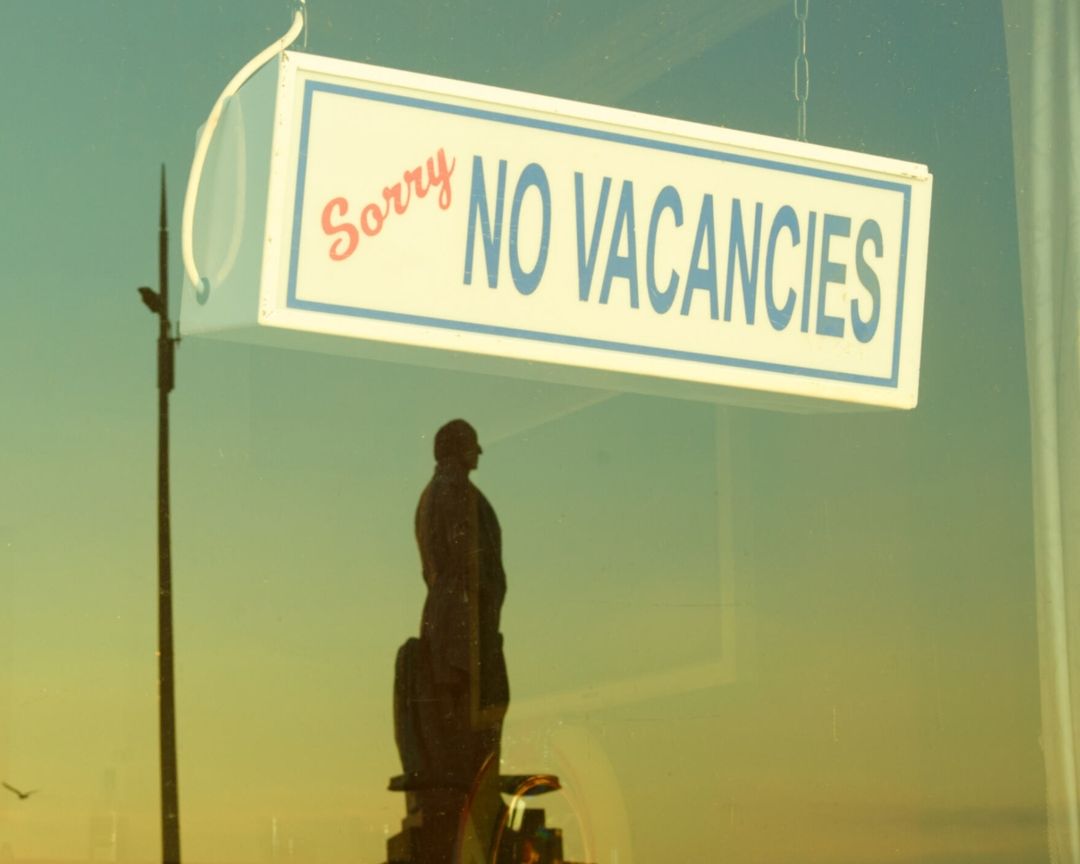 Vintage photograph through a window of a 'Sorry, No Vacancies' sign hanging with a statue visible through the glass.