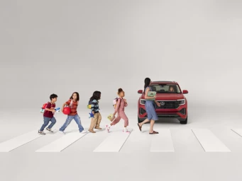 A line of children and a woman walking across a crosswalk in front of a red SUV on a white seamless background