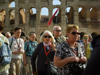Group of tourists walking in front of the Colosseum in Rome, with a tour guide holding a small red and white flag.