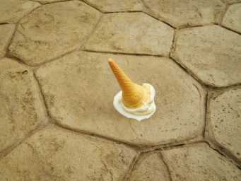 Dropped ice cream cone upside down on textured stone paving slabs with melted vanilla scoop