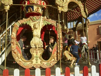 Vintage carousel with ornate wooden carvings, red and white striped canopy, and people riding on children's horses.