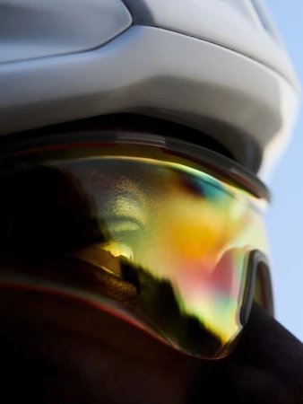 Close-up of a person wearing a white helmet and iridescent goggles reflecting a landscape against a clear blue sky