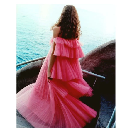 Woman in a tiered pink tulle dress seen from behind standing by the ocean