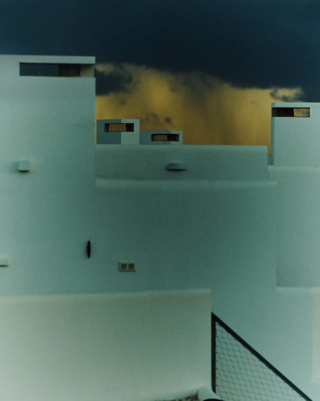 Low-angle shot of stark white buildings against a dramatic cloudy sky, creating a minimalist architectural landscape with cool, muted tones.