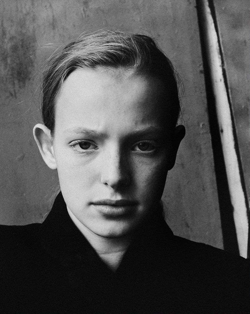 Close-up black and white portrait of a young person wearing a dark collared shirt against a textured background.