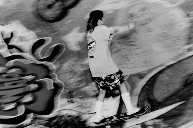 Monochrome action shot of a skateboarder in motion against a graffiti covered wall by Daniel Benson