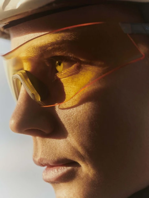 Close-up portrait of a fair-skinned adult wearing yellow-tinted sunglasses and a white helmet in the sun, showcasing sport and fitness.