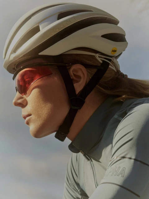 Profile shot of an adult female cyclist wearing a helmet and sunglasses, with focus on her face, gear, and sportswear.