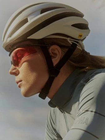 Profile shot of an adult female cyclist wearing a helmet and sunglasses, with focus on her face, gear, and sportswear.