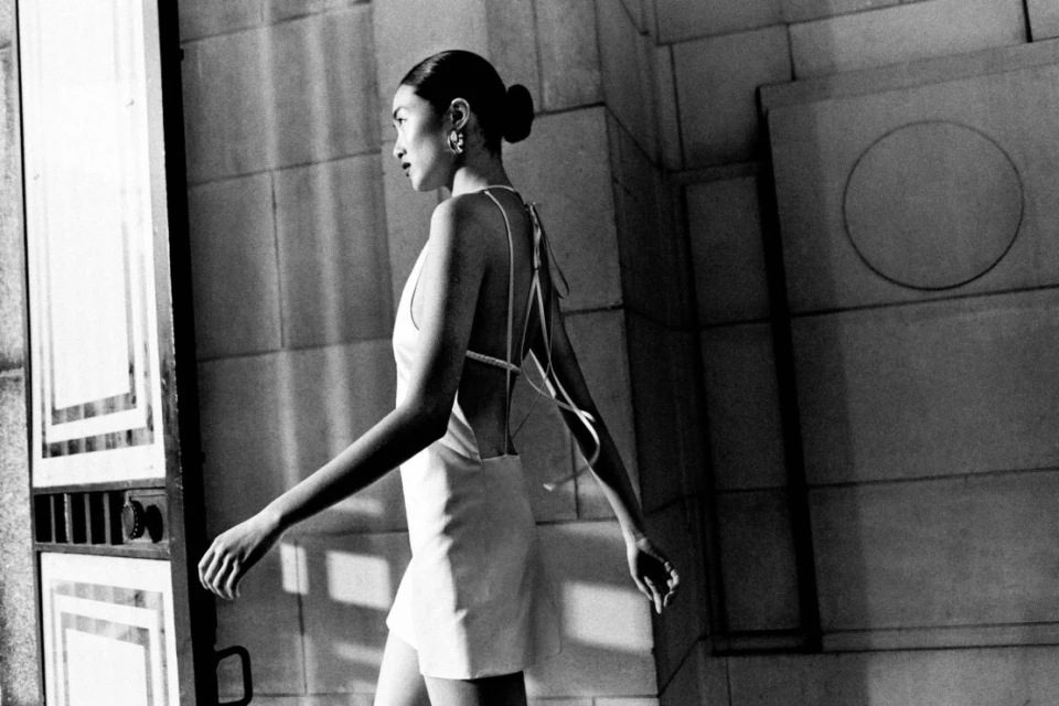 Monochrome fashion portrait of an Asian woman walking in a short dress, featuring architectural details and a minimalist aesthetic.