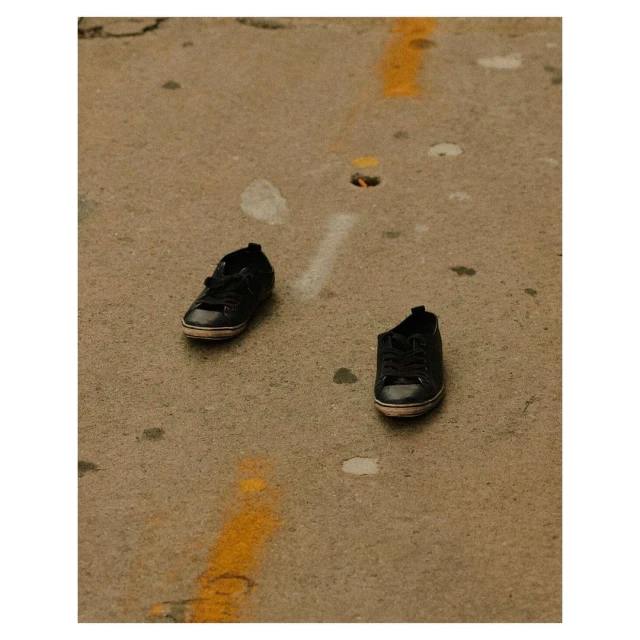 Two black shoes sit on a concrete ground with a yellow line. The footwear is isolated in the frame on the dirty surface.