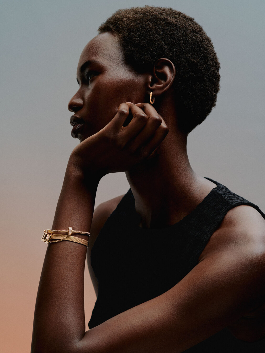 Profile portrait of a Black woman wearing gold hoop earrings and a bracelet, captured in soft lighting by Daniel Benson in London.