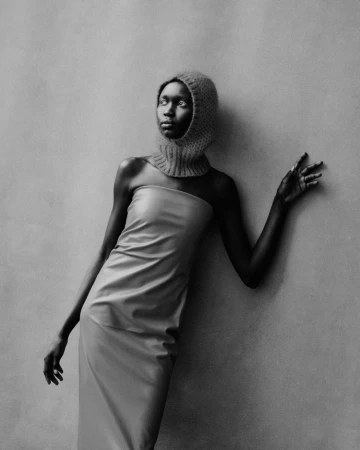 Elegant black and white studio portrait of a woman in a textured hood and a draped dress, gazing off-camera in a fashion-forward pose.