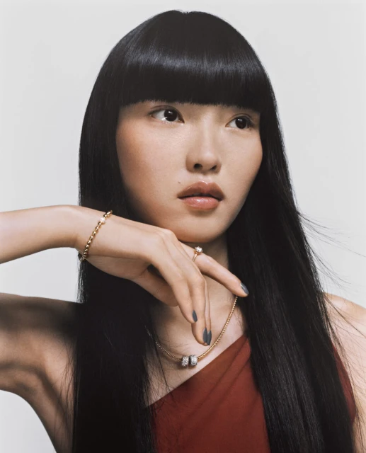 Headshot of an Asian woman with black hair in red top wearing gold jewelry against a light background in a fashion style