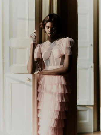 Woman in pale pink tiered tulle dress standing by an open white paneled door with natural light.