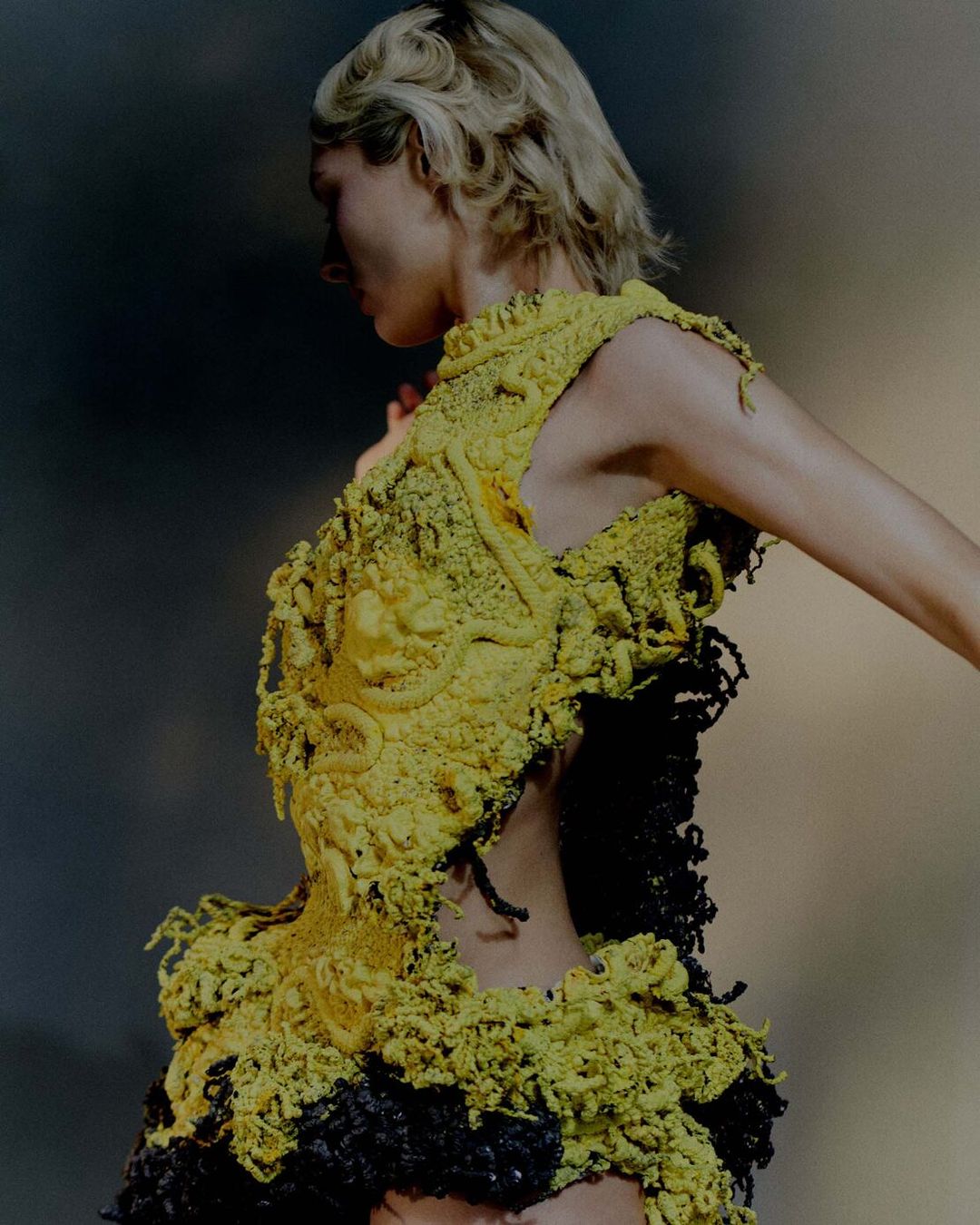 Fashion shot of a woman in a textured yellow and black dress against a neutral background, showcasing avant-garde design and unique textures.
