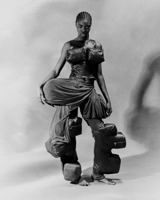 Black and white studio shot of African American woman in avant-garde puffy fashion, unusual silhouette, full body, stark lighting.