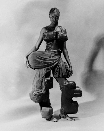 Black and white studio shot of African American woman in avant-garde puffy fashion, unusual silhouette, full body, stark lighting.