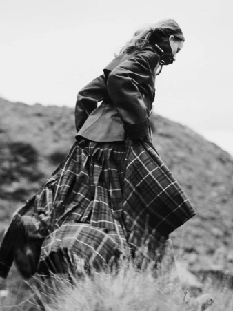 Model in dark jacket and plaid skirt walking outdoors on a rough terrain by Daniel Benson