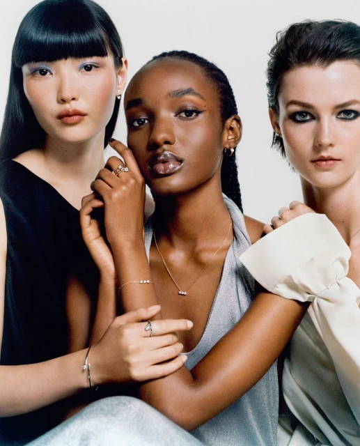 Three women pose in a studio wearing jewelry, including necklaces, rings, bracelets and earrings. The background is a solid white.