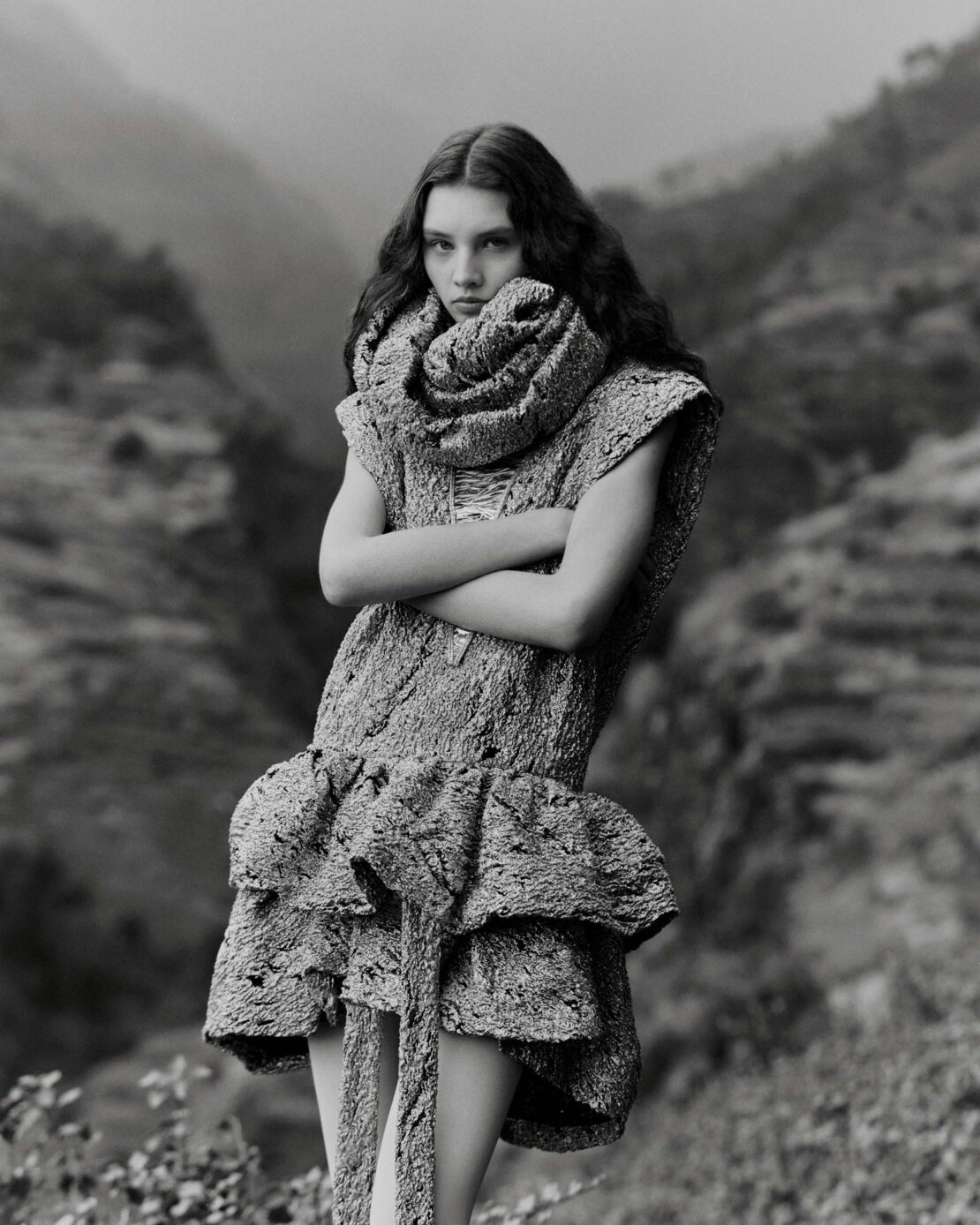 Monochrome portrait of a young woman with long dark wavy hair wearing a textured patterned dress and a large matching rolled collar scarf
