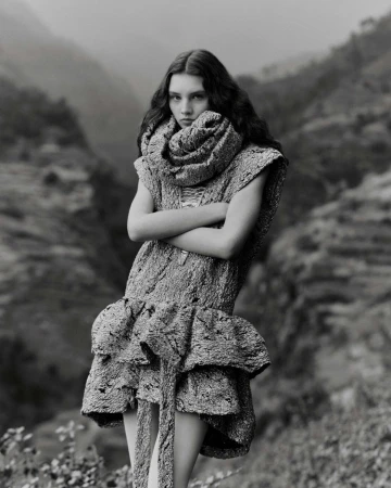 Monochrome portrait of a young woman with long dark wavy hair wearing a textured patterned dress and a large matching rolled collar scarf