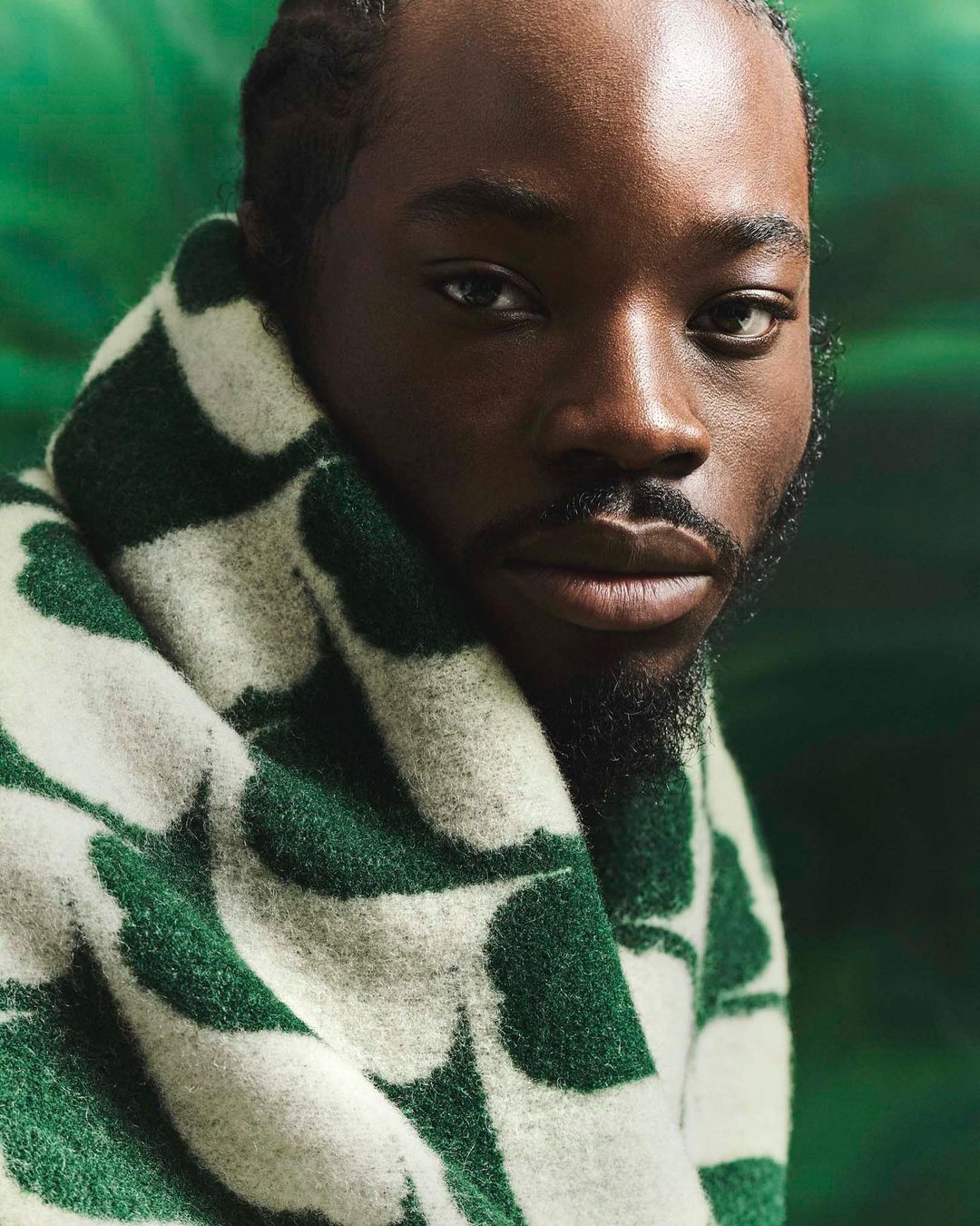 Close-up studio shot of an African-American adult male with dark hair and a trimmed beard, wrapped in a patterned shawl, looking at camera.