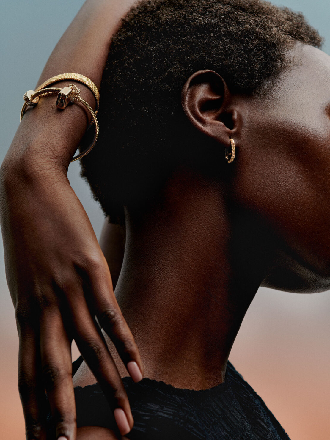 Close up profile portrait of a black woman wearing gold bracelets and small hoop earrings by Daniel Benson.