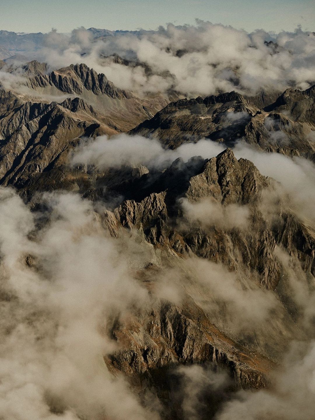 Scenic aerial view of rugged mountain peaks partially covered in clouds. Landscape shot of rocky, steep terrain and atmospheric sky.