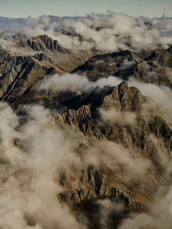 Scenic aerial view of rugged mountain peaks partially covered in clouds. Landscape shot of rocky, steep terrain and atmospheric sky.