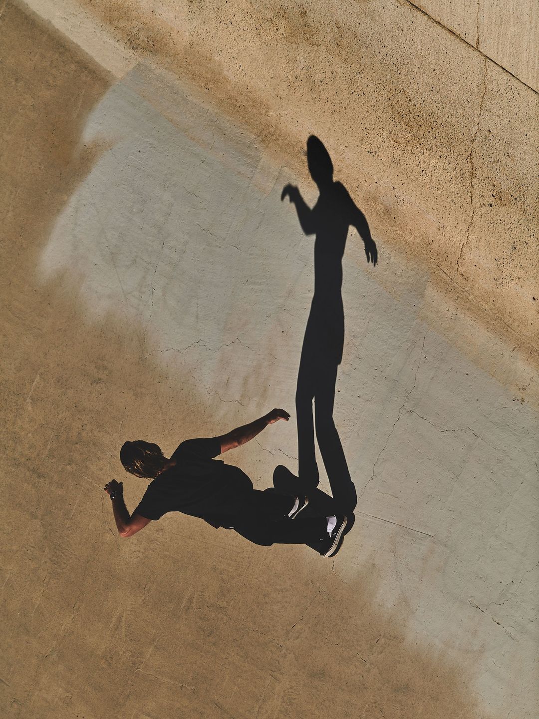 Top-down view of two human shadows cast on the ground, one lying down, the other standing with a light source overhead.