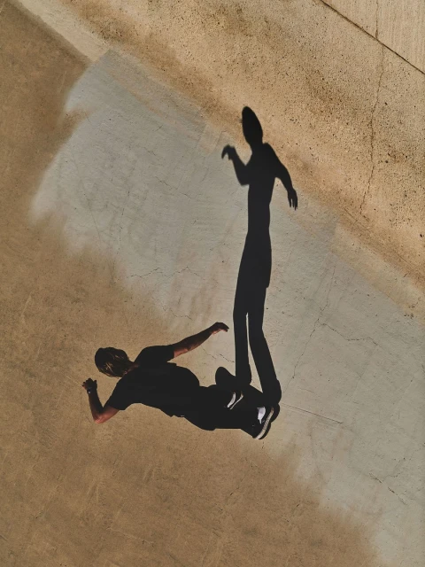 Top-down view of two human shadows cast on the ground, one lying down, the other standing with a light source overhead.